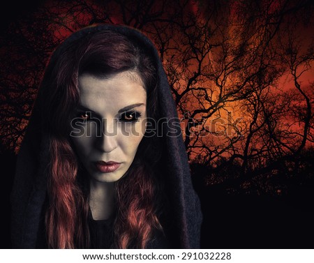 Portrait of a witch with scary eyes and a wood on fire in background.
