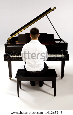 Man with Grand piano wearing white shirt and black pants sitting at piano bench.