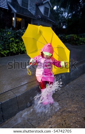 Little girl with yellow umbrella playing in rain wearing pink rain slicker and pink galoshes