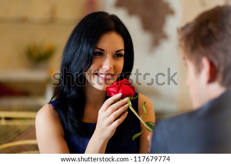 Young happy couple romantic date at restaurant, celebrating valentine day man give red rose to his girl