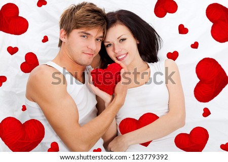 love valentine day couple holding red heart together lying in a bed, man and woman happy smile looking at camera, concept hearts flying around