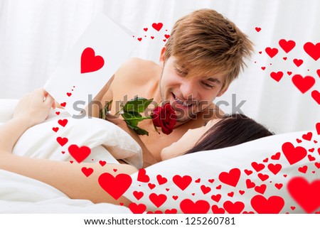 love valentine day couple lying in bed, Man giving a rose, greeting card to his beautiful wife in bed, happy smile looking to each other, concept hearts flying around