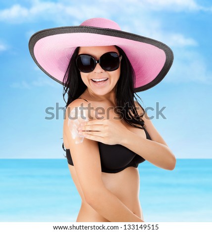 woman smile moisturizing applying sun cream on her tanned arm hands, summer vacation beach, sun tanned body, girl wear pink hat, sunglasses, over sea blue sky, concept holiday travel