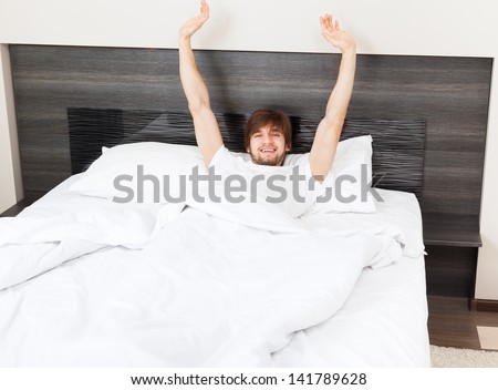 Handsome man lying waking up stretching and yawning lying on bed, happy smile morning wake up, attractive guy smiling in bedroom at home, sexy young male model