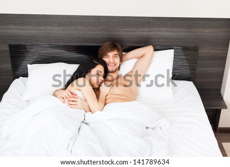 young couple in bed, happy smile man embrace love, woman sleep with closed eyes lying in bedroom