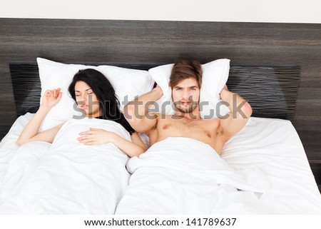 Couple in bed, snoring woman, man can not sleep, covering ears with pillow for snore noise, sleeping in bedroom at home.