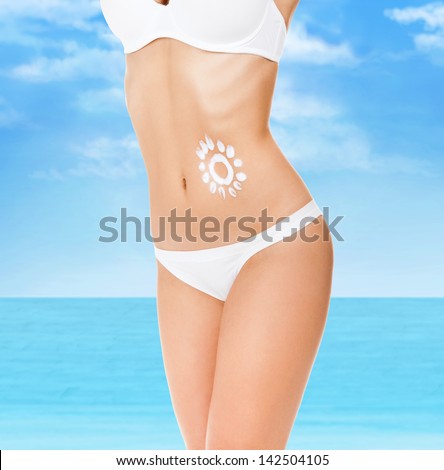 Sunscreen lotion over tan woman belly skin made as sun shape, concept of skin care health applying cream on tanned body, sunny vacation holiday blue sky