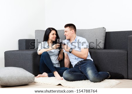 young couple drink red wine toast, sitting on floor near sofa happy smile, lovely young man and woman love, romantic celebrate hold glass, at couch in living room