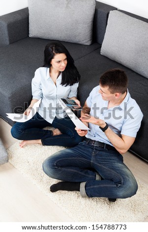 Unhappy couple reading a letter in the living room, hold calculator, sitting on floor near couch, sofa worried, concept of negative bill, money finance problem calculating bills, top angle view