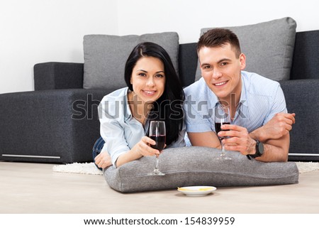 young couple drink red wine toast, lying on floor near sofa happy smile, lovely young man and woman love, romantic celebrate hold glass, at couch in living room