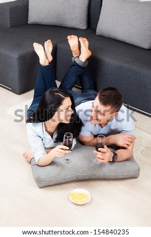 young couple drink red wine, lying on floor near sofa happy smile, lovely young man and woman love, romantic celebrate hold glass toast, at couch in living room, top angle view