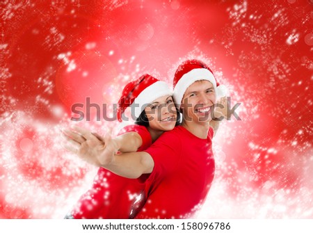 christmas holiday couple love smiling with hands outstretched lifted upwards, man and woman smile wear red shirts and new year hat, over abstract magic winter background with sparkles blowing snow