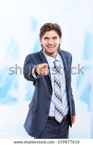 young business man point finger at you happy smile in bright blue office, Handsome businessman wear elegant suit and tie