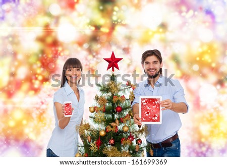 christmas holiday happy couple hold present cell phone tablet pad computer, show touch screen, new year decorated tree, family man and woman smile over abstract colorful lights background