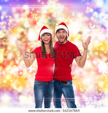 christmas holiday couple excited happy smile hold palm arm hand up gesture, in red new year hat, man and woman smile, over abstract colorful lights background