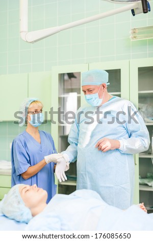 Surgery team in operating room with patient, nurse help doctor wear glove in hospital ward