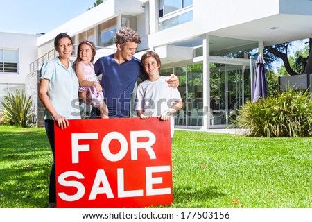 Beautiful family portrait standing outside their new house smiling, hold for sale sign