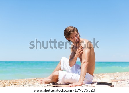 man apply sunscreen protection lotion on back tanned body, sitting on summer beach travel ocean vacation, concept of applying skin care sun protect