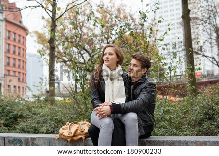 Young woman sitting on man\'s lap while looking away on parapet