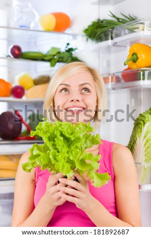 young woman hold fresh green salad diet think look up, refrigerator open door, pretty ponder girl dieting dream healthy food vegetables and fruits