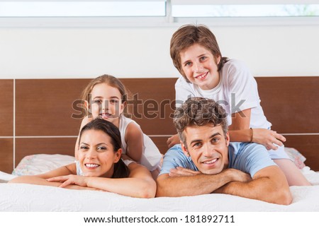 Happy family lying on a bed together in the bedroom, young couple parents smile with children on top of each other