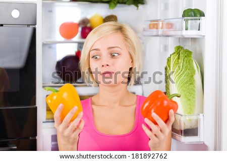girl unhappy look to red yellow pepper, near refrigerator open door, diet healthy food, young woman sad vitamin vegetables negative emotion