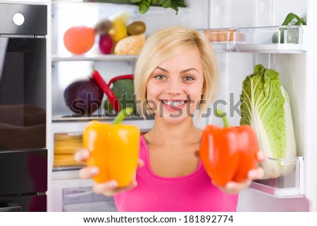 pretty girl hold red yellow pepper, near refrigerator open door, diet healthy food concept, young woman smile vitamin vegetables