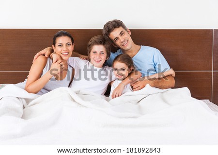 Happy family sitting on a bed together in the bedroom, young couple parents smile embrace with children