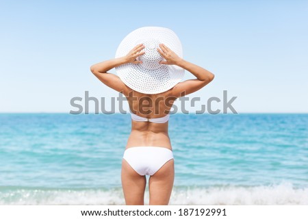 Woman on beach, Rear view of young beautiful girl wearing summer hat and bikini, standing back looking to sea blue sky horizon, vacation concept of travel ocean