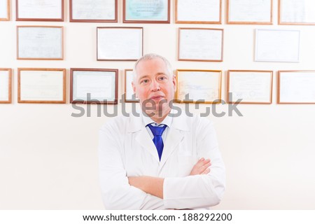 doctor white coat, folded hands over office wall with certificate background