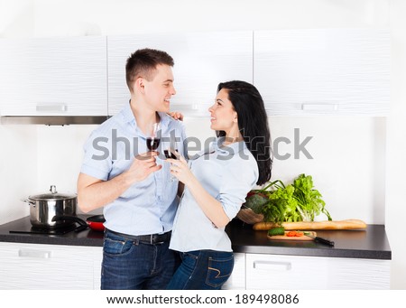 couple drink red wine toast at their kitchen home, happy smile, lovely looking to each other young man and woman love, romantic embrace celebrate hold glass