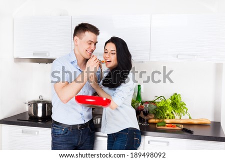 couple tasting the meal in their kitchen happy smile, man feed woman with spoon, cooking at home