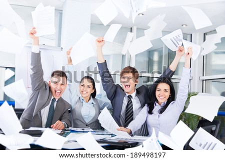 business people excited happy smile, throw papers, documents fly in air, businesspeople sitting at office desk hold hands arms up, success team concept after sign contract