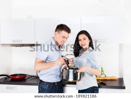 couple cooking in their home kitchen happy smile, man woman holding pan with spoon