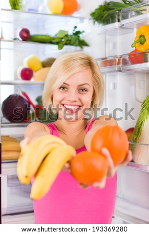 young woman hold banana orange in hands near open door refrigerator, concept of diet health food, pretty girl hold vitamin fruit