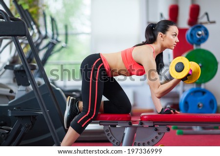 Woman in gym sport exercising with dumbbells lifting weights, young girl working out on her biceps