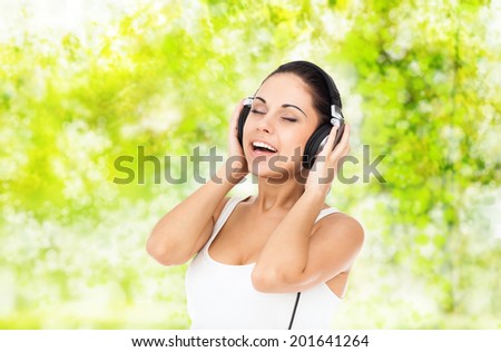 woman in headphones listen to music smile sing closed eyes over gree tree park outdoor background