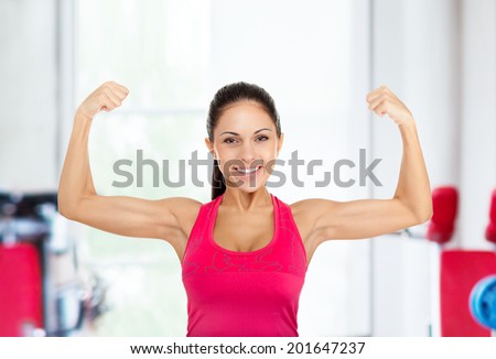 sport fitness woman flexing show her biceps muscles, young healthy smile girl athletic body, perfect figure in gym