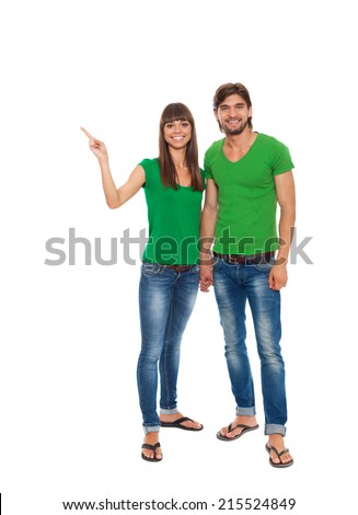 beautiful young happy couple love smiling embracing point finger to empty copy space, man and woman smile wear green t shirt jeacns full length portrait, isolated over white background