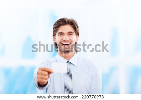 Business man happy smile holding a blank business card, give visiting, credit card, dressed in elegant shirt over blue office background