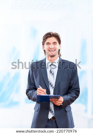 Handsome young business man happy smile writing on clipboard sign up contract in bright blue office, businessman wear elegant suit and tie