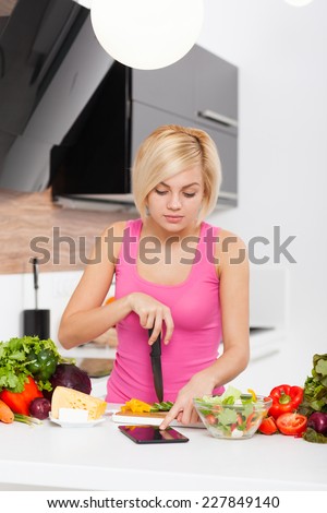 Blonde woman using a tablet computer to cook in modern kitchen, young girl fresh raw vegetables cooking at home smile