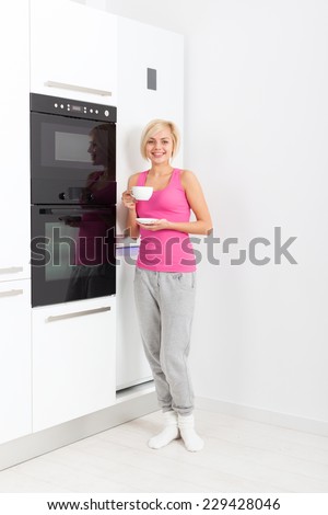 young girl drink coffee, woman smile standing at modern bright white kitchen appliance