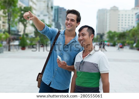 Two men tourists smile point finger sightseeing, asian mix race friends guys outdoor city street