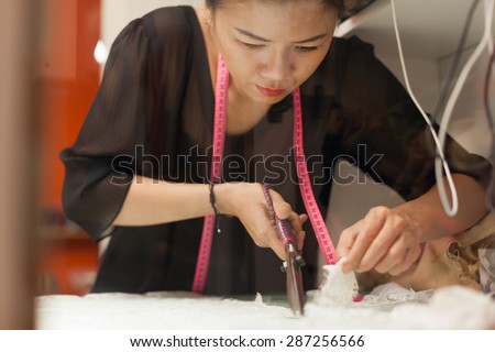 Asian woman tailor fashion clothes dress designer working with scissors fabric on table