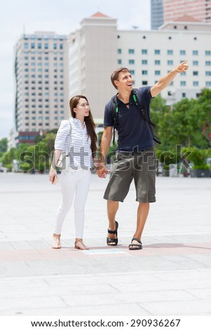 Couple asian girl and caucasian man tourist smile point finger sightseeing, mix race friends outdoor city street