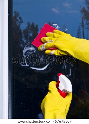 Female hand in pink glove cleaning window with yellow microfibre