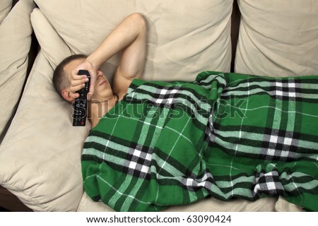 A young man sleeping on the couch with remote control