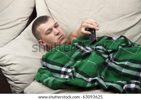 casual man, lying on the couch, watching television with the command at hand