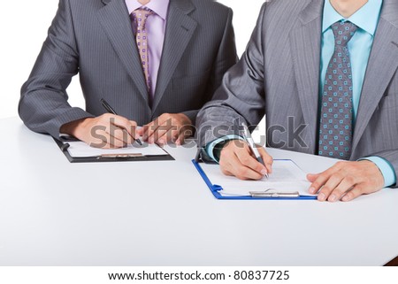 Two business people in elegant suits sitting at desk working in team together, working with documents sign up contract, on clipboard, folder with papers, business plan. Isolated over white background.